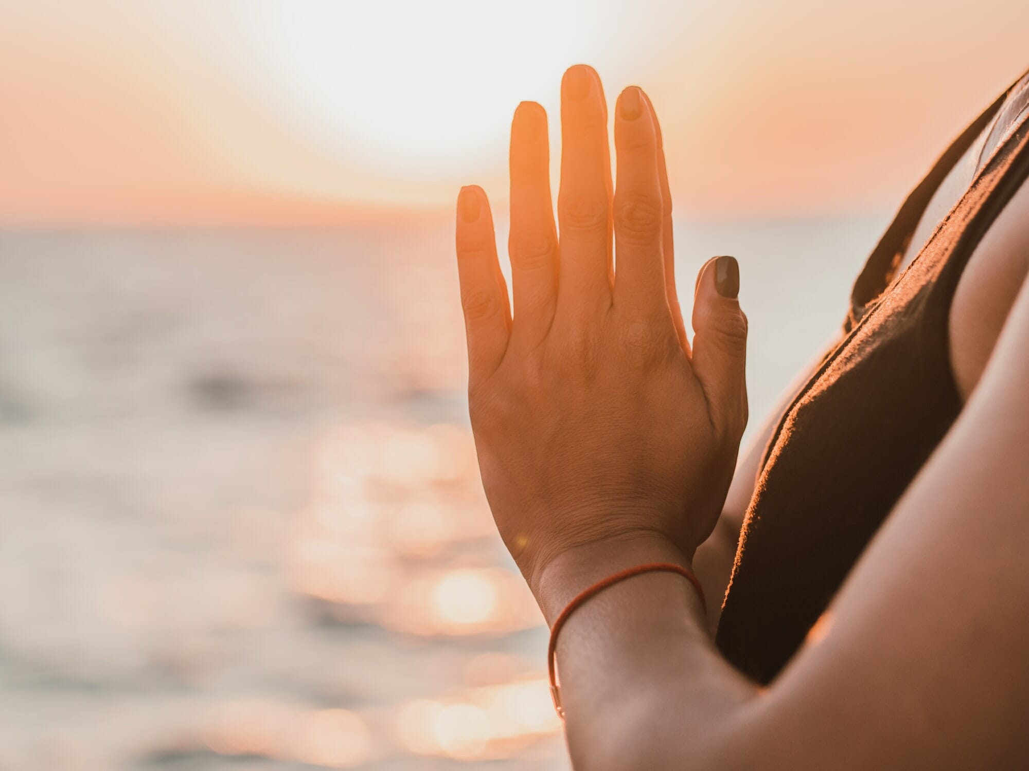 Pleasant woman makes greeting to the sun at sunrise on sea coast. Hands in namaste. Yoga
